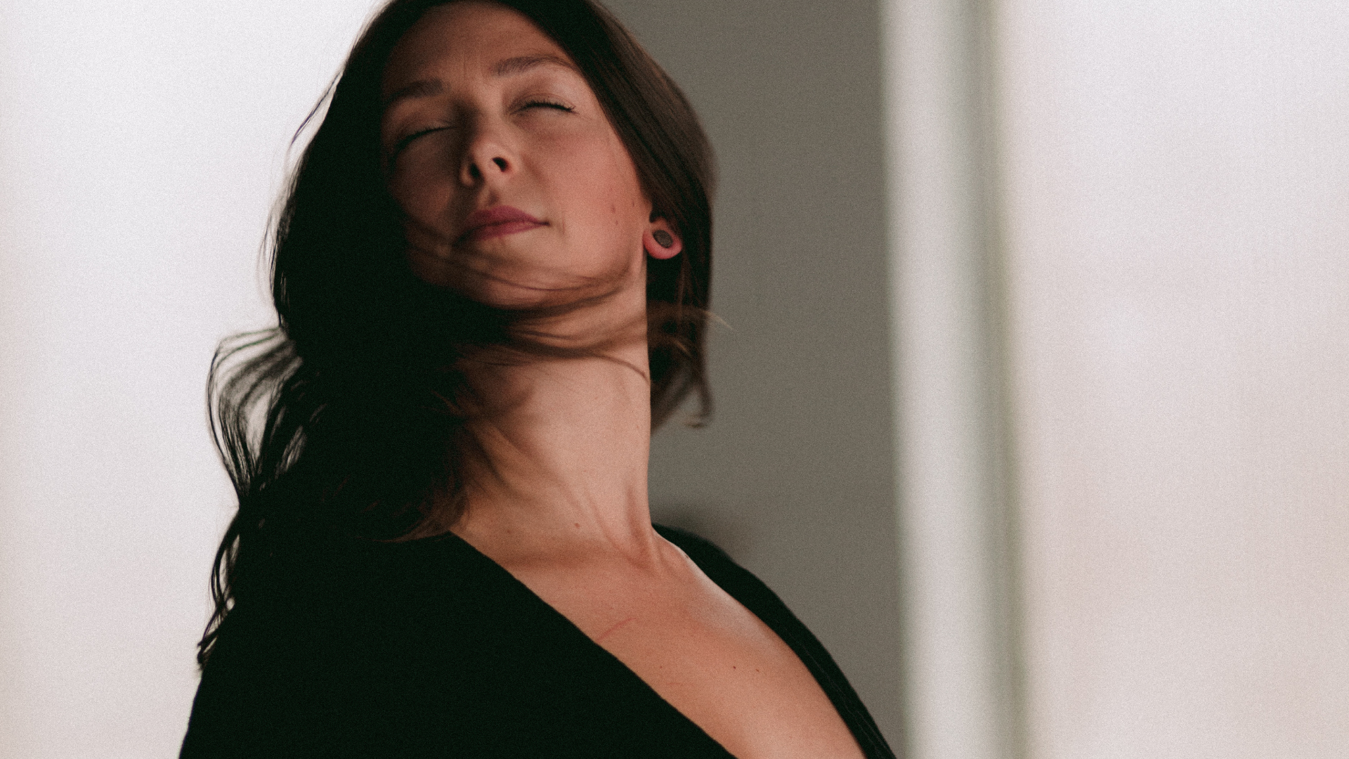Naomi Elder embodiment coach in motion dancing portrait with eyes closed hair sweeping across her face wearing black