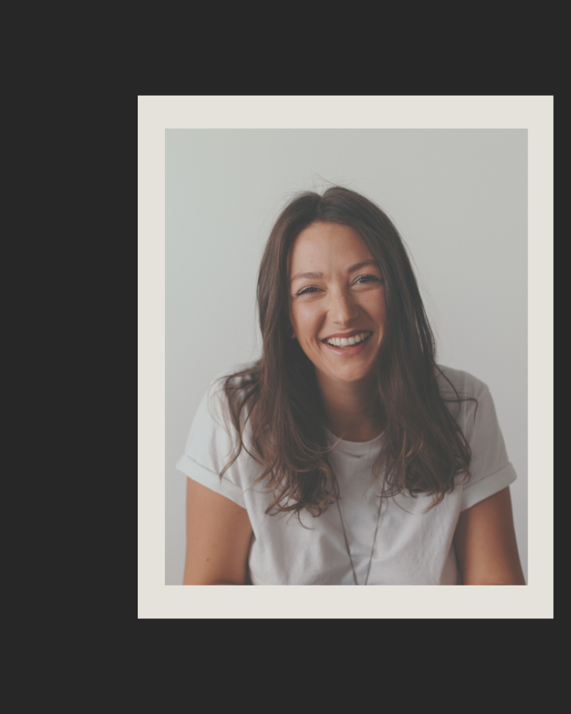 portrait of coach Naomi Elder sitting upright smiling with long dark hair, wearing a white t-shirt 